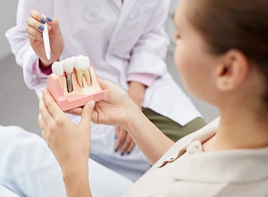 Dentist pointing to sample implant patient is holding