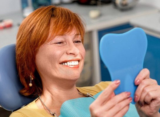 Patient admiring her new smile in small dental mirror