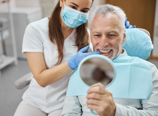 Dentist touching man’s teeth as he smiles at reflection in handheld mirror