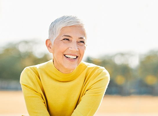 Senior woman in yellow shirt sitting outside and smiling