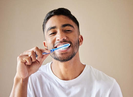 Smiling patient in white shirt brushing their teeth