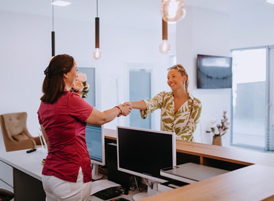 Dental receptionist and patient shaking hands in lobby