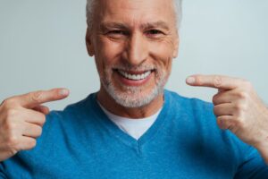 Senior man smiling and pointing towards dentures.