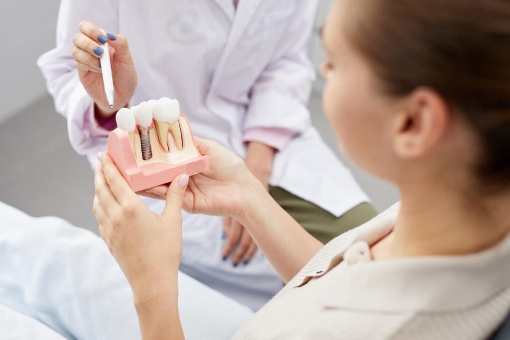 a patient holds a model of dental implants while dentist explains to her the procedure