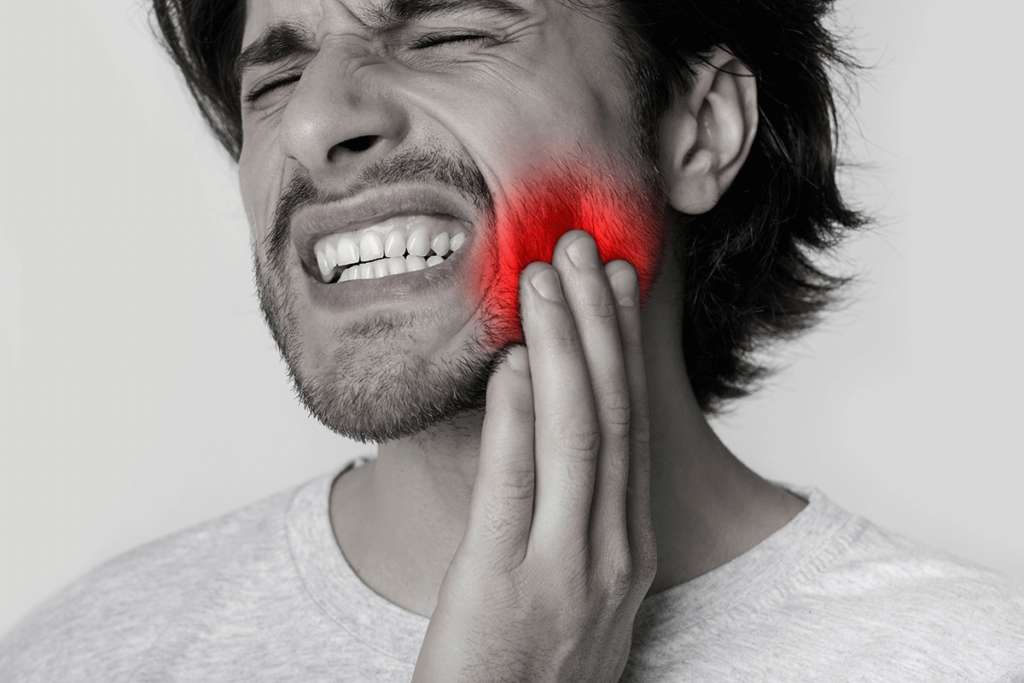 a man appears to be excruciating pain in his mouth and holds his hand to his jaw wondering what is a dental emergency