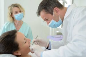 a patient gets work done from an emergency dentist while a dental assistant watches nearby