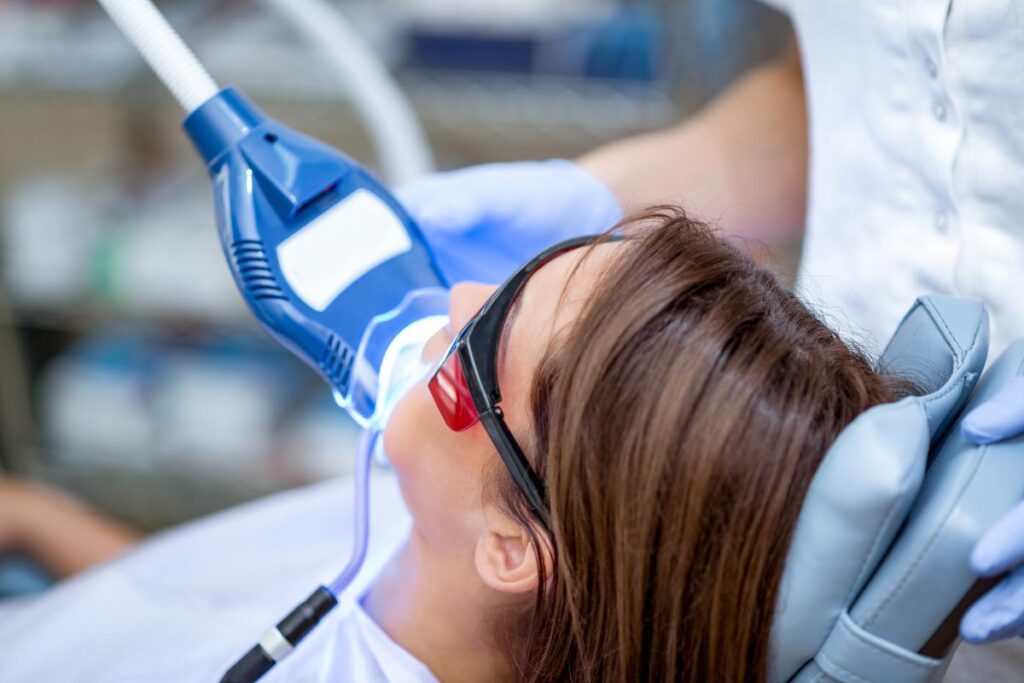 a patient sits in a dental exam chair and receives teeth whitening services after the dentist asks her question about is teeth whitening harmful