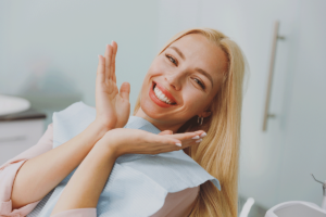 a blonde woman patient smiles and holds hands near her face focusing on her new smile showing examples of restorative dentistry