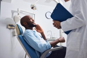 male patient leans back in a dental exam chair and asks his dentist about a tooth extraction cost